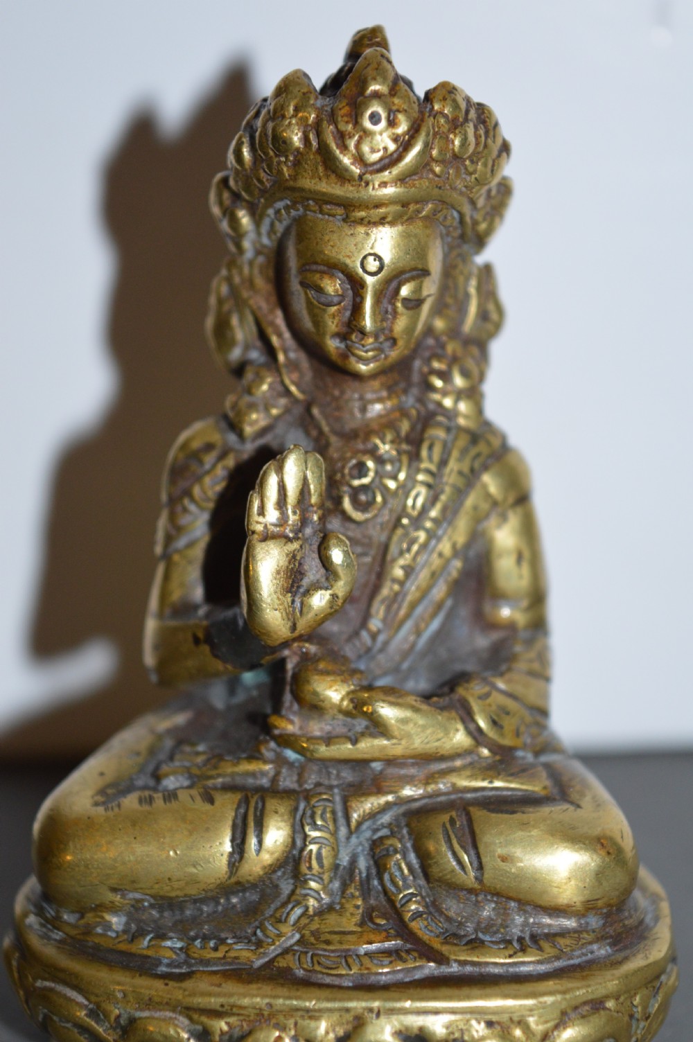 A 19th-century Tibetan bronze figure depicting a crowned seated Buddha in lotus position with a raised hand.