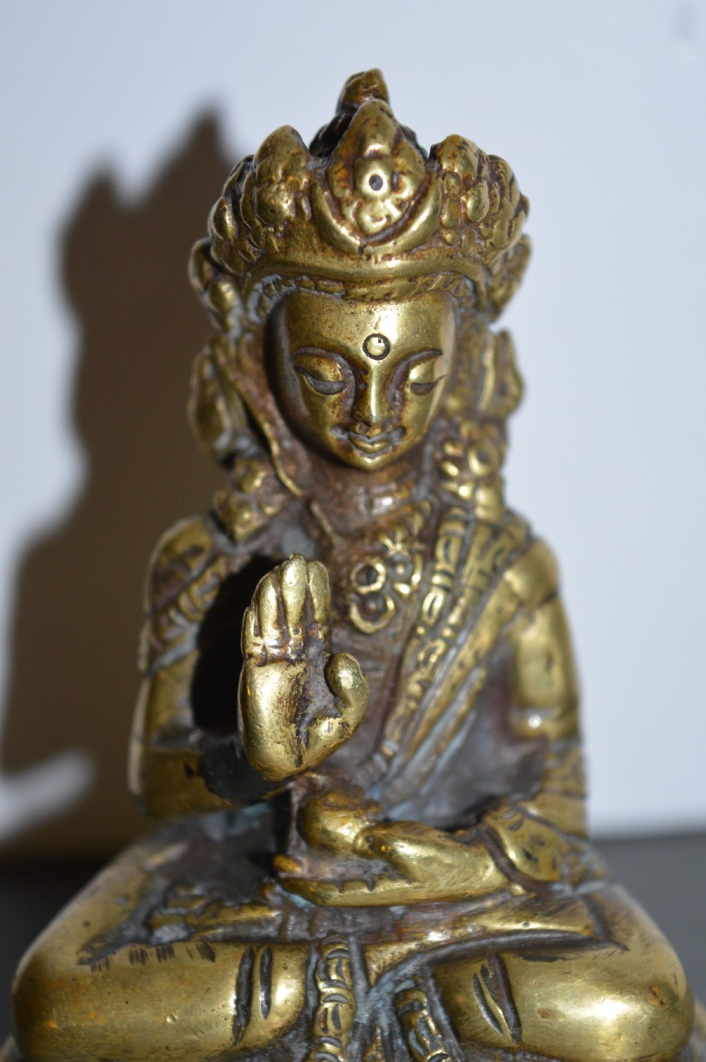 A 19th-century Tibetan bronze figure depicting a crowned seated Buddha in lotus position with a raised hand. View III