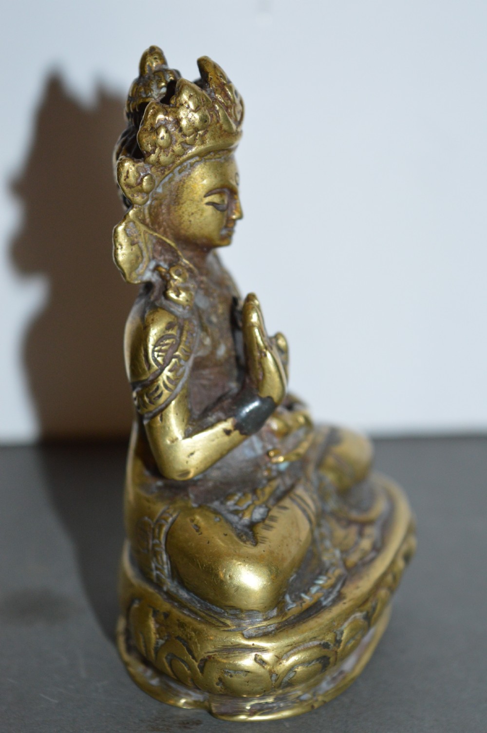 A 19th-century Tibetan bronze figure depicting a crowned seated Buddha in lotus position with a raised hand. View IV