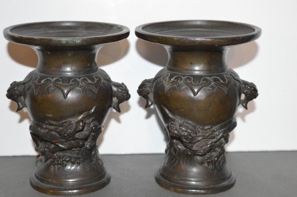 A pair of dark brown cast bronze Chinese vases featuring high-relief dragon motifs, beast head handles, and wide dished rims.