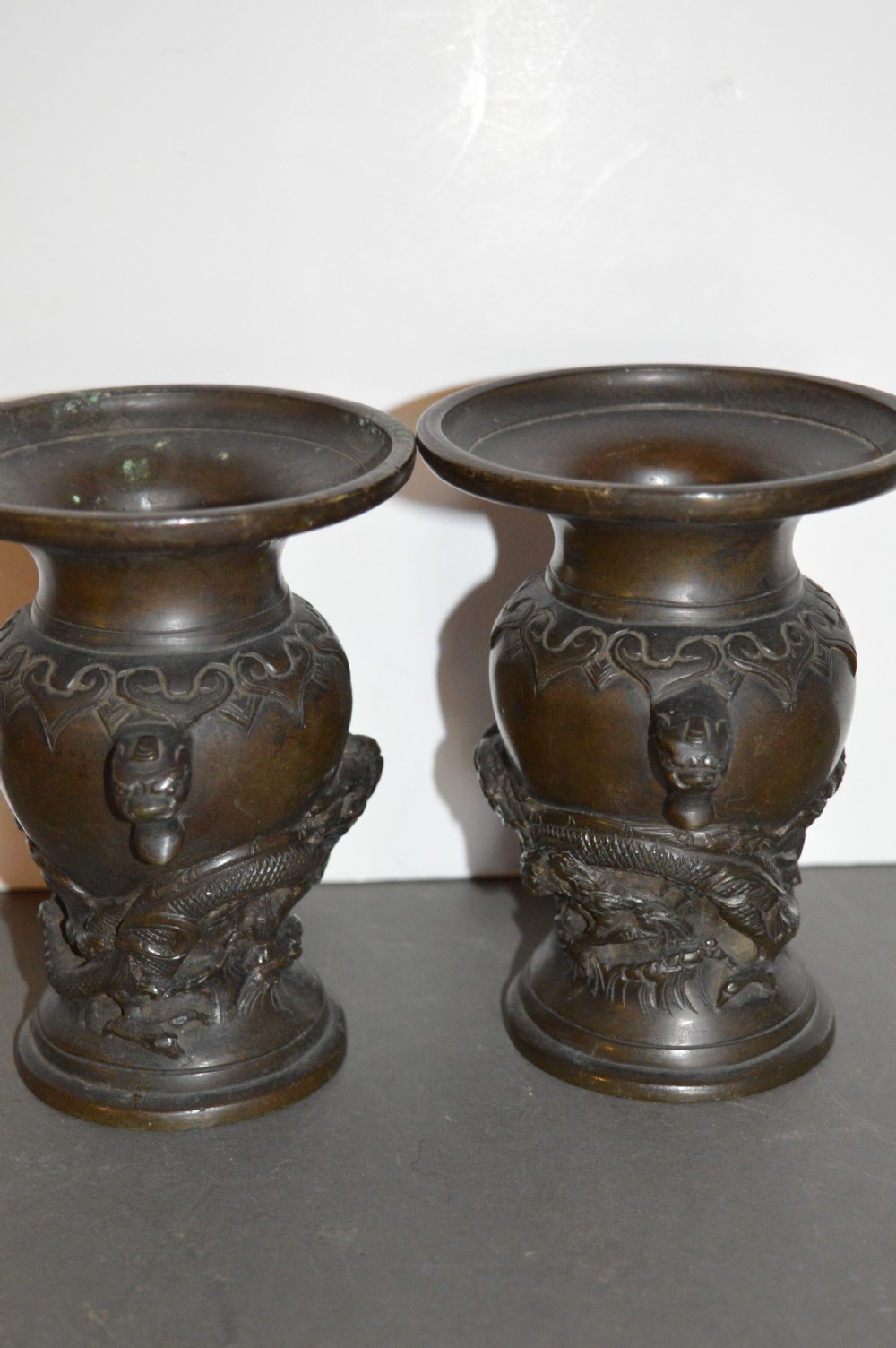A pair of dark brown cast bronze Chinese vases featuring high-relief dragon motifs, beast head handles, and wide dished rims. View V