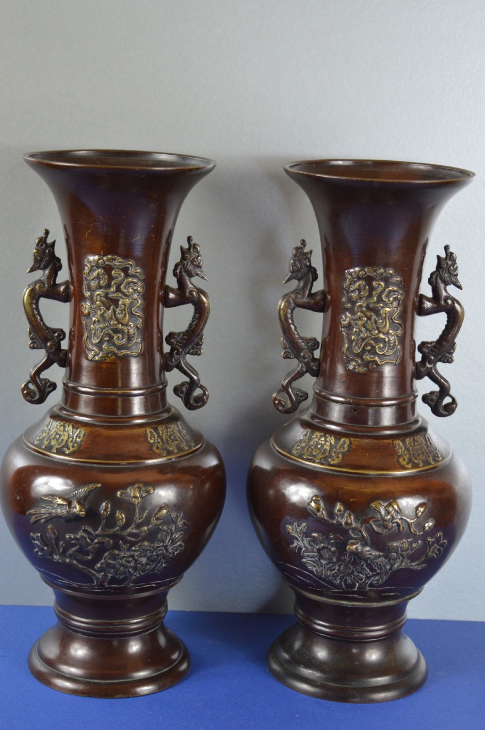 A pair of patinated dark brown Chinese bronze baluster vases with dragon handles and relief floral carvings.