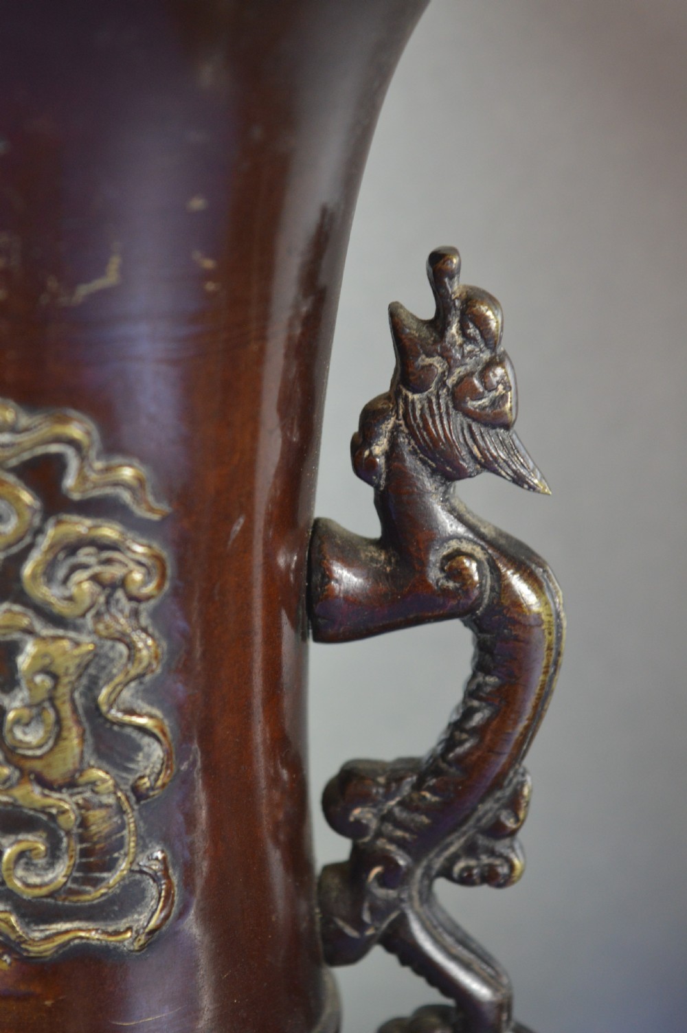 A pair of patinated dark brown Chinese bronze baluster vases with dragon handles and relief floral carvings. View V