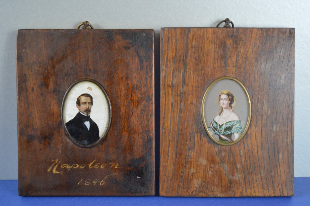 A pair of rectangular wooden plaque frames holding oval hand-painted portrait miniatures of Napoleon and Empress Eugenie within brass bezels.