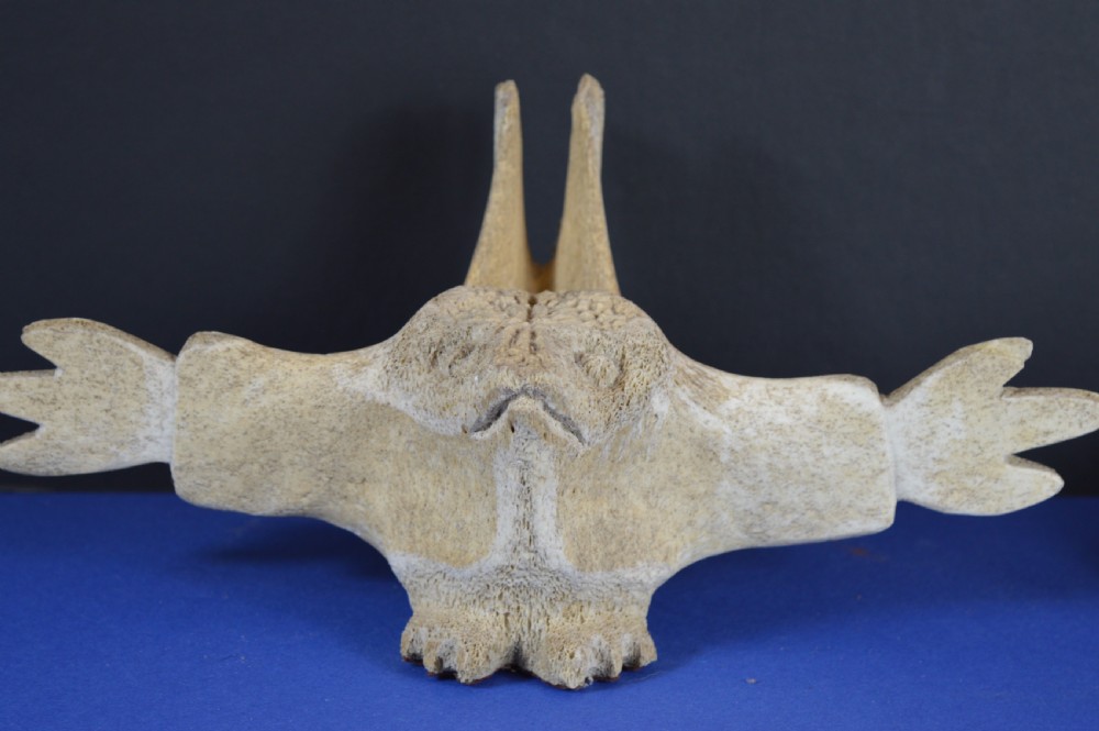 A carved whale vertebra figure with extended side limbs, stylized facial features, and a textured bone surface.