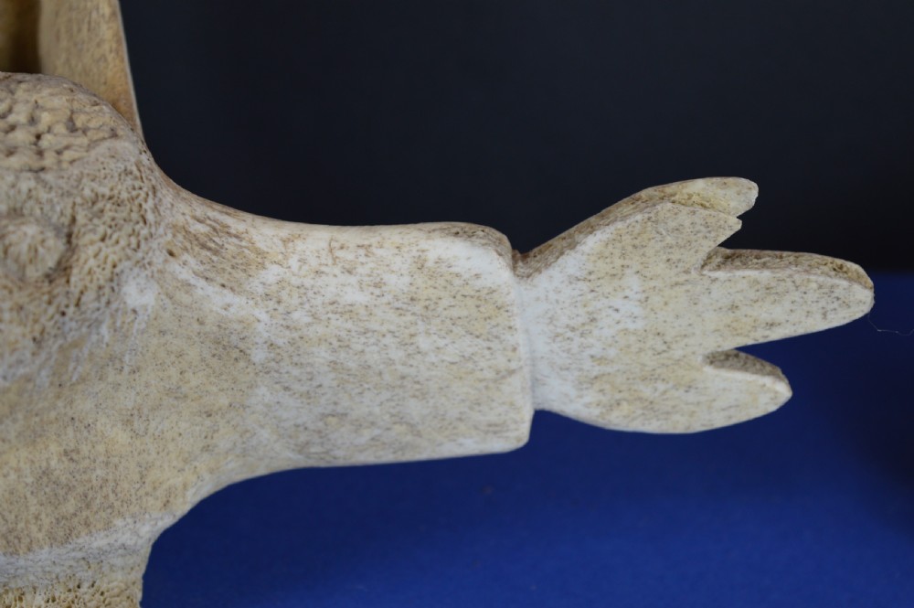 A carved whale vertebra figure with extended side limbs, stylized facial features, and a textured bone surface. View III