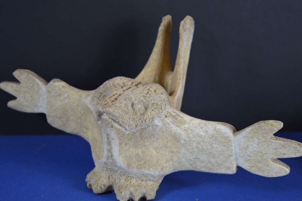 A carved whale vertebra figure with extended side limbs, stylized facial features, and a textured bone surface. View VII