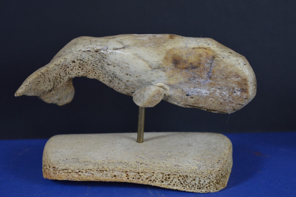 A hand-carved whale figure made from porous whalebone mounted on a metal pin above a rectangular bone plinth base. View II