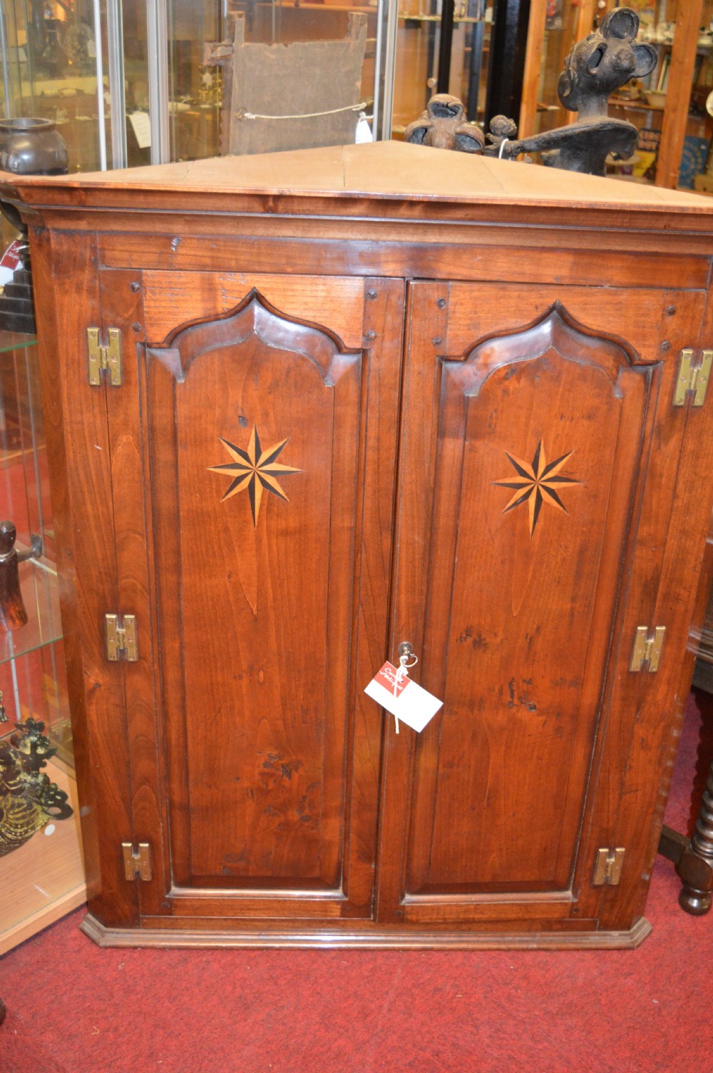 A nineteenth-century mahogany corner hanging cupboard featuring twin panelled doors with inlaid star motifs and brass H-hinges.