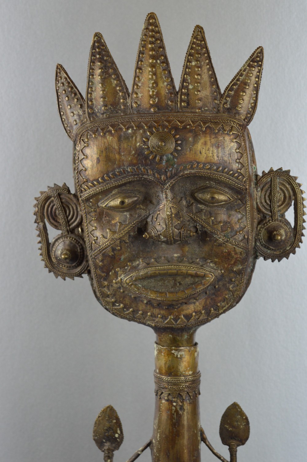 A tall, cast brass African statue featuring a stylized king figure with a spiked crown, elaborate facial details, and a tapered cylindrical base. View II
