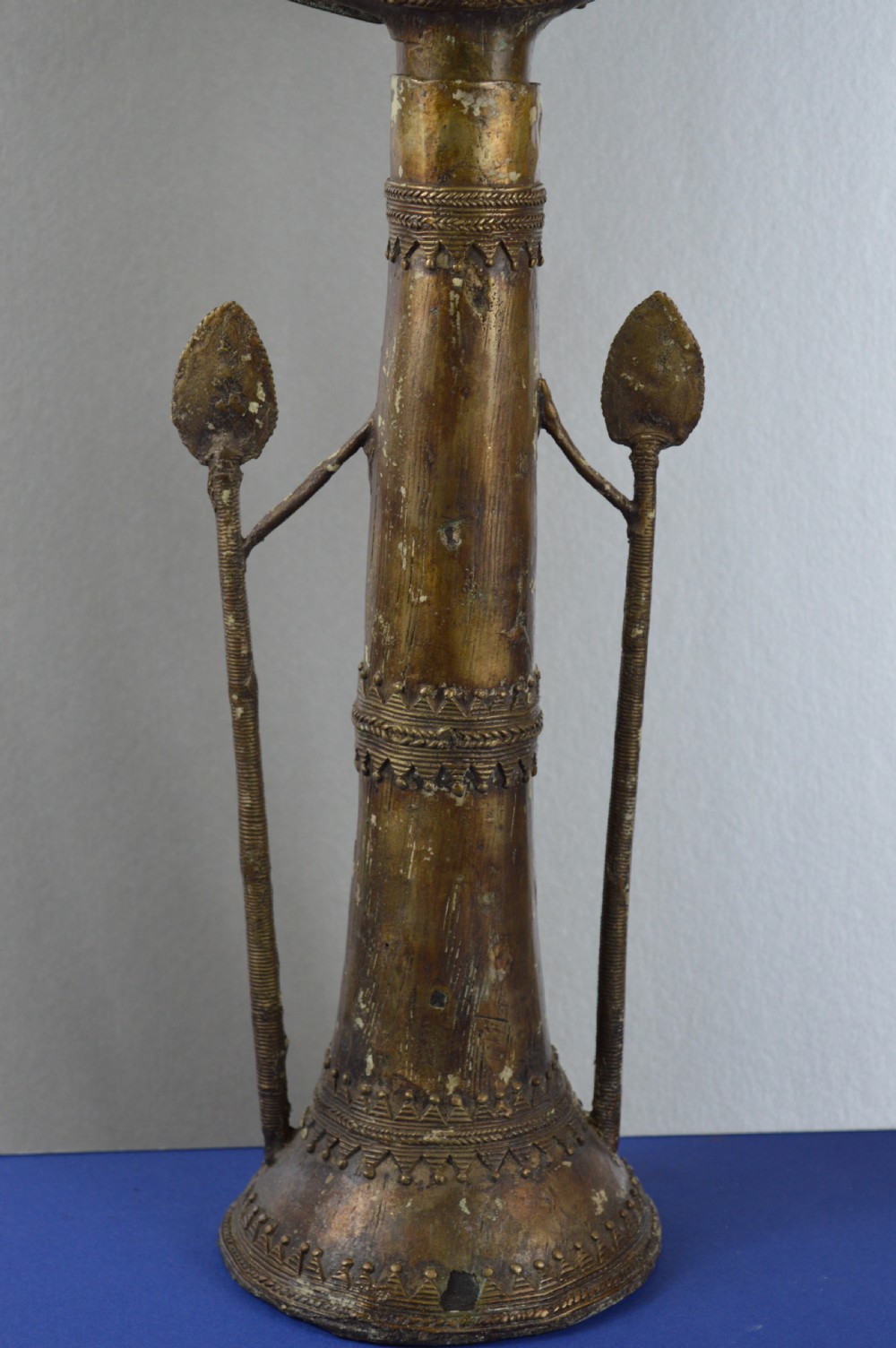 A tall, cast brass African statue featuring a stylized king figure with a spiked crown, elaborate facial details, and a tapered cylindrical base. View III