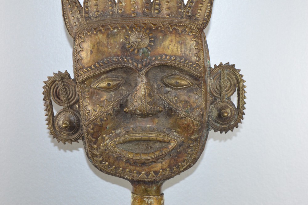 A tall, cast brass African statue featuring a stylized king figure with a spiked crown, elaborate facial details, and a tapered cylindrical base. View IV