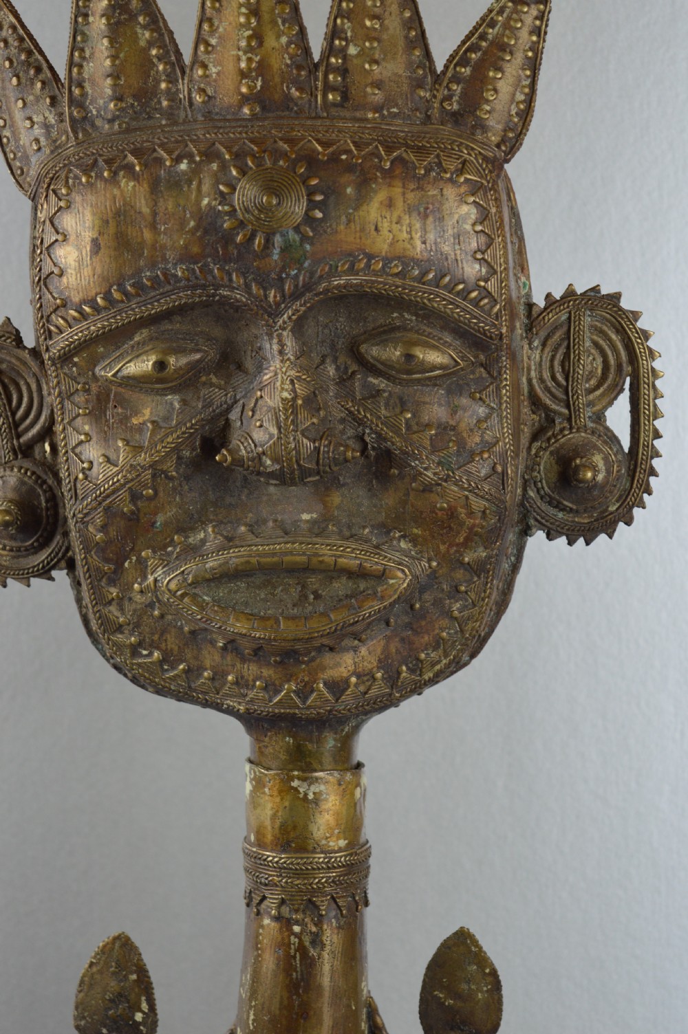 A tall, cast brass African statue featuring a stylized king figure with a spiked crown, elaborate facial details, and a tapered cylindrical base. View V