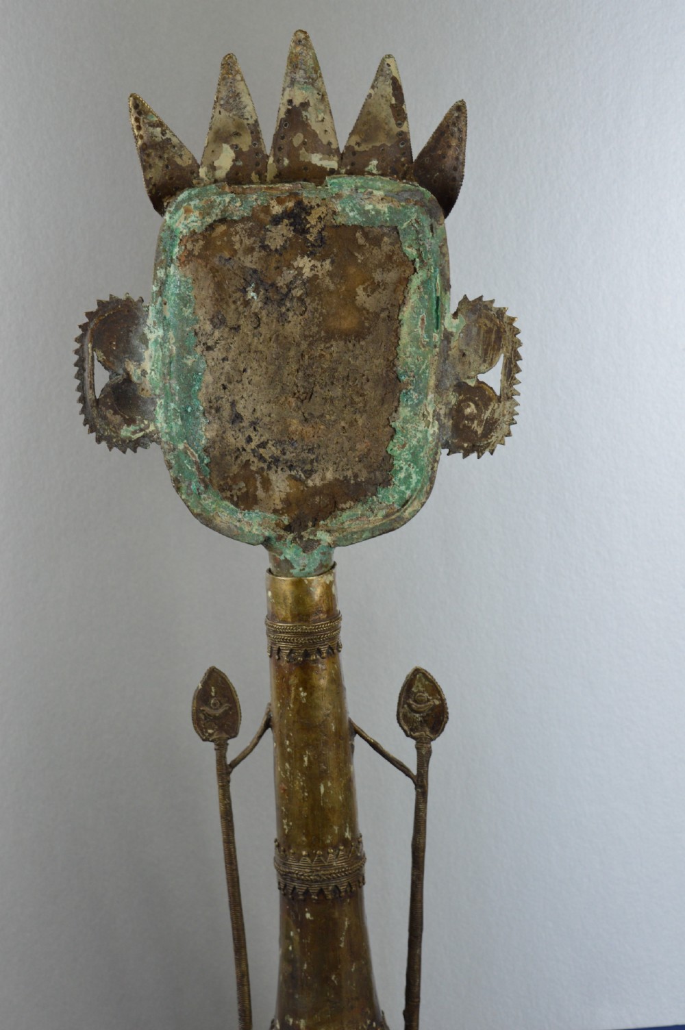 A tall, cast brass African statue featuring a stylized king figure with a spiked crown, elaborate facial details, and a tapered cylindrical base. View IX