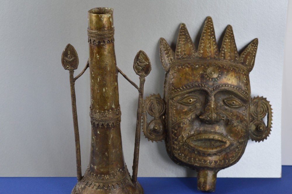 A tall, cast brass African statue featuring a stylized king figure with a spiked crown, elaborate facial details, and a tapered cylindrical base. View XI