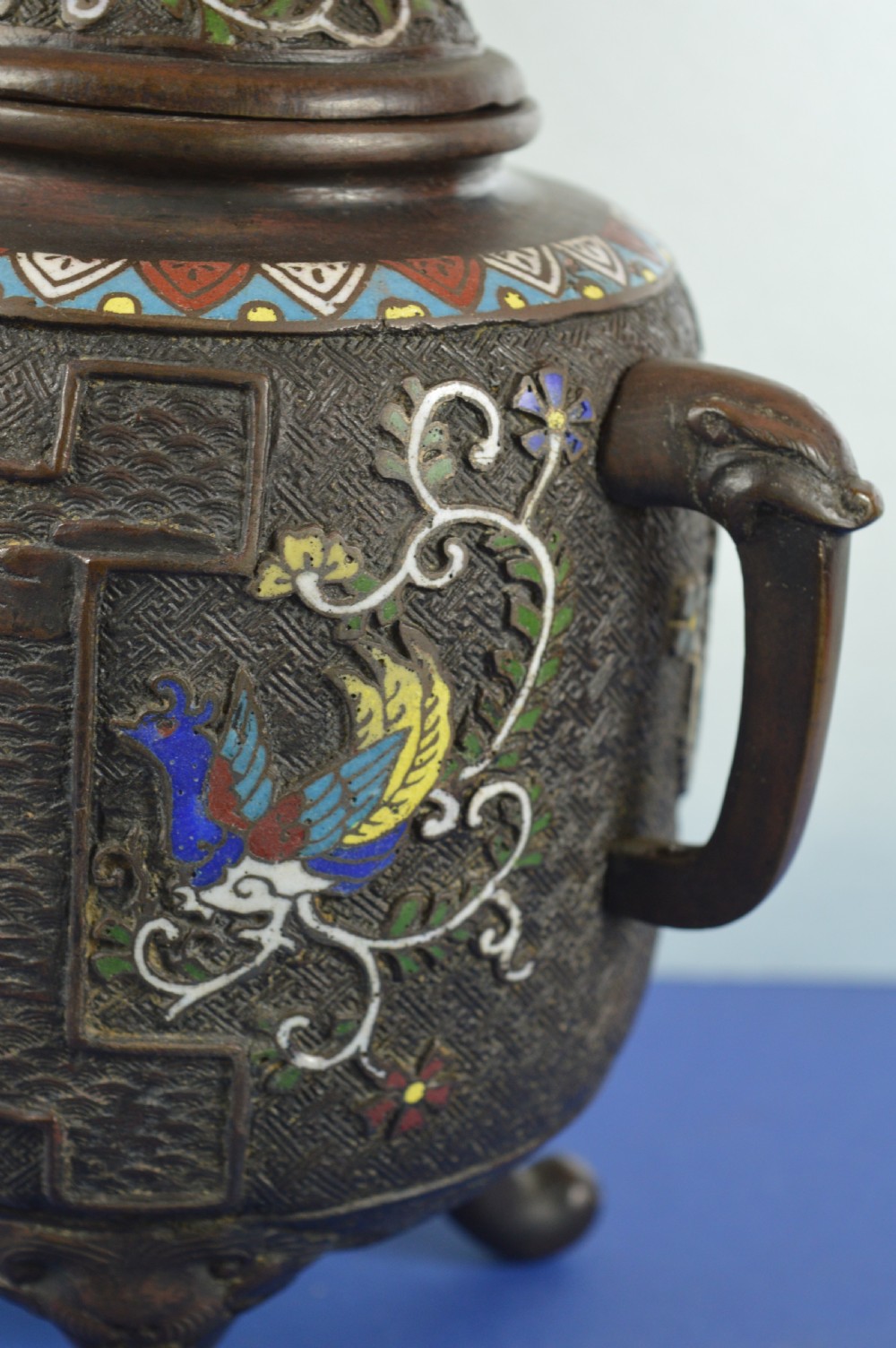 A late nineteenth-century Japanese bronze tripod censer featuring polychrome cloisonne enamel work, relief panels depicting a sailboat, loop handles, and a cover topped with a beast finial. View V