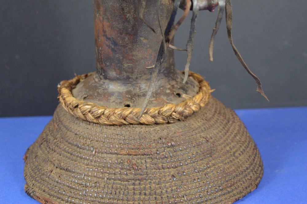 A tall dark bronze Yoruba head displaying facial scarification, a high conical helmet, leather beard attachments, and a woven rope base. View IV