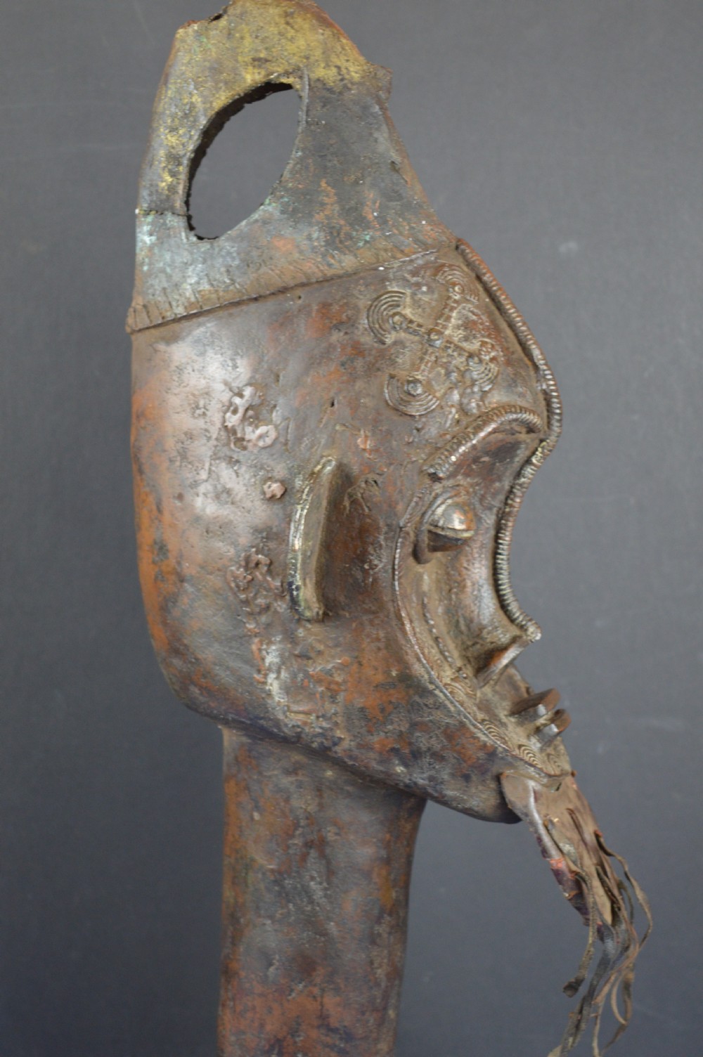 A tall dark bronze Yoruba head displaying facial scarification, a high conical helmet, leather beard attachments, and a woven rope base. View VI