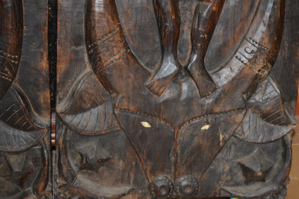 Pair of dark hand-carved wooden doors featuring high-relief human figures holding roosters above water buffalo heads with bone inlaid eyes. View VI