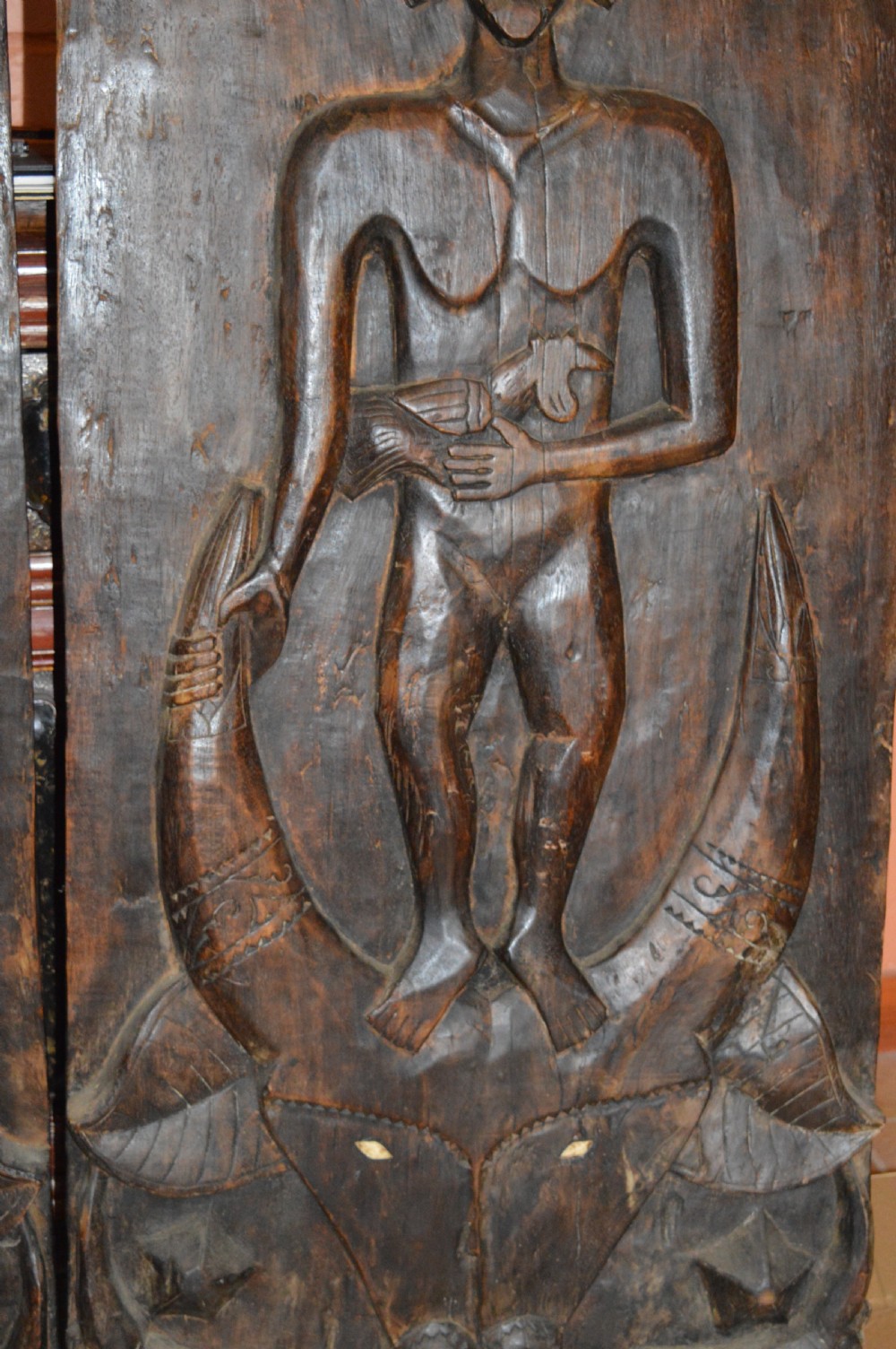 Pair of dark hand-carved wooden doors featuring high-relief human figures holding roosters above water buffalo heads with bone inlaid eyes. View VIII