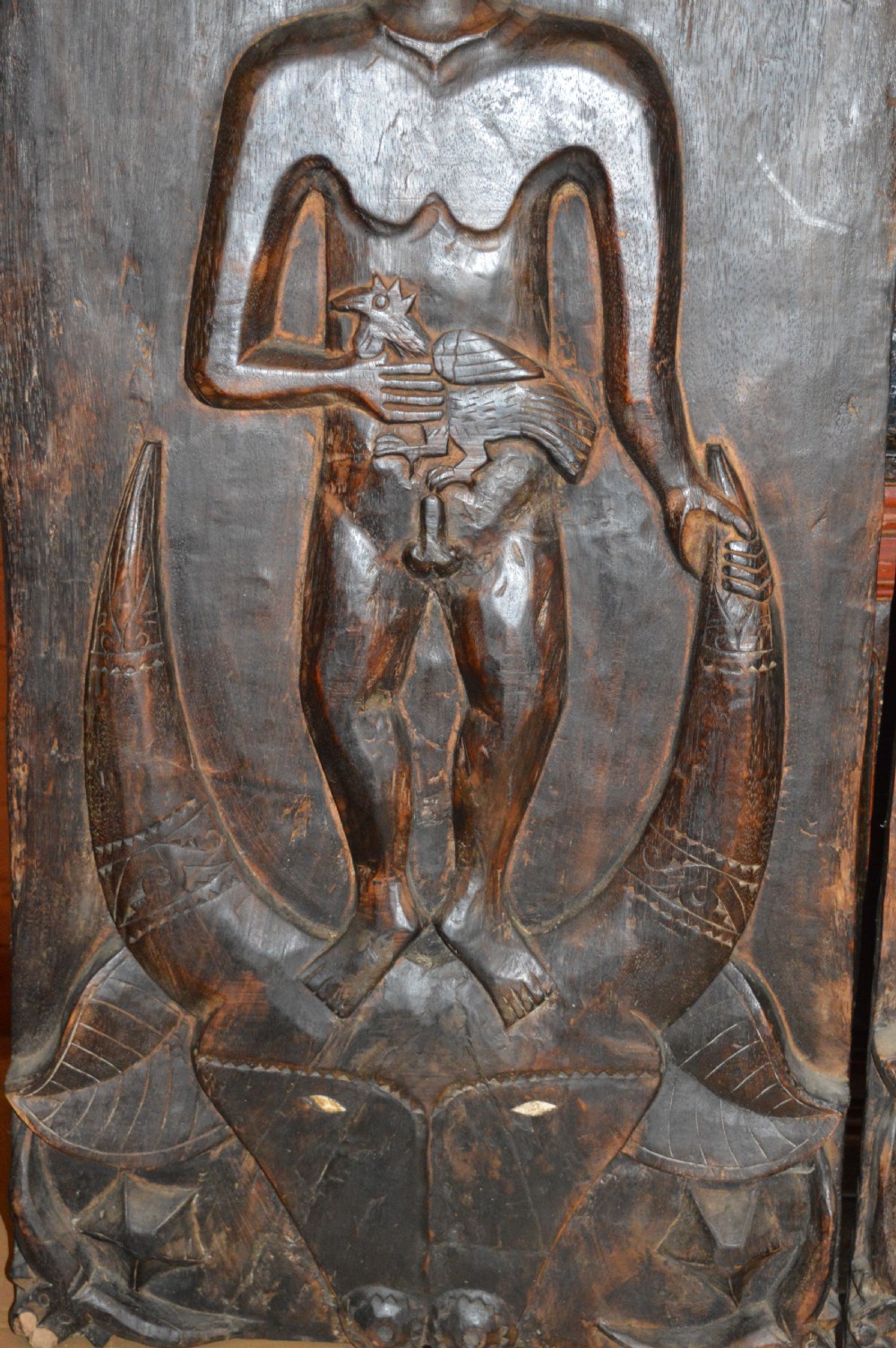Pair of dark hand-carved wooden doors featuring high-relief human figures holding roosters above water buffalo heads with bone inlaid eyes. View IX