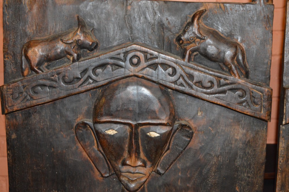 Pair of dark hand-carved wooden doors featuring high-relief human figures holding roosters above water buffalo heads with bone inlaid eyes. View XIII