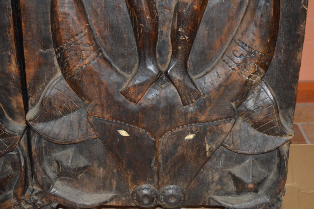Pair of dark hand-carved wooden doors featuring high-relief human figures holding roosters above water buffalo heads with bone inlaid eyes. View XV