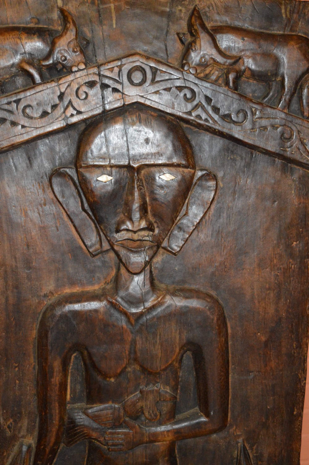 Pair of dark hand-carved wooden doors featuring high-relief human figures holding roosters above water buffalo heads with bone inlaid eyes. View XVI