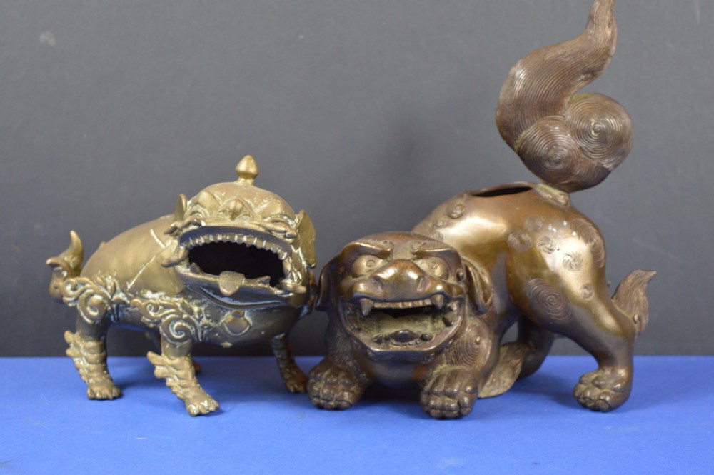 A pair of antique cast bronze Chinese foo dog incense burners with carved scroll details and open mouths.