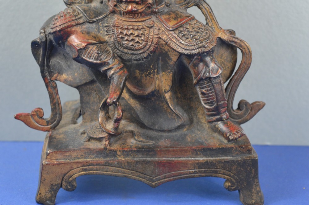 A late nineteenth-century Chinese dark bronze sculpture depicting a seated warrior in detailed armour with polychrome red accents and a decorative halo motif. View II