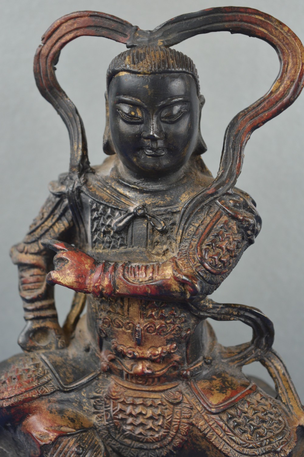 A late nineteenth-century Chinese dark bronze sculpture depicting a seated warrior in detailed armour with polychrome red accents and a decorative halo motif. View III