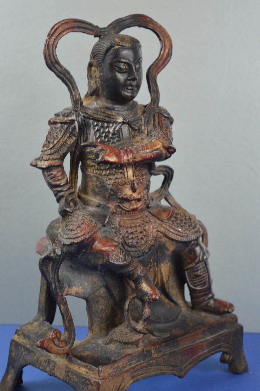 A late nineteenth-century Chinese dark bronze sculpture depicting a seated warrior in detailed armour with polychrome red accents and a decorative halo motif. View IV
