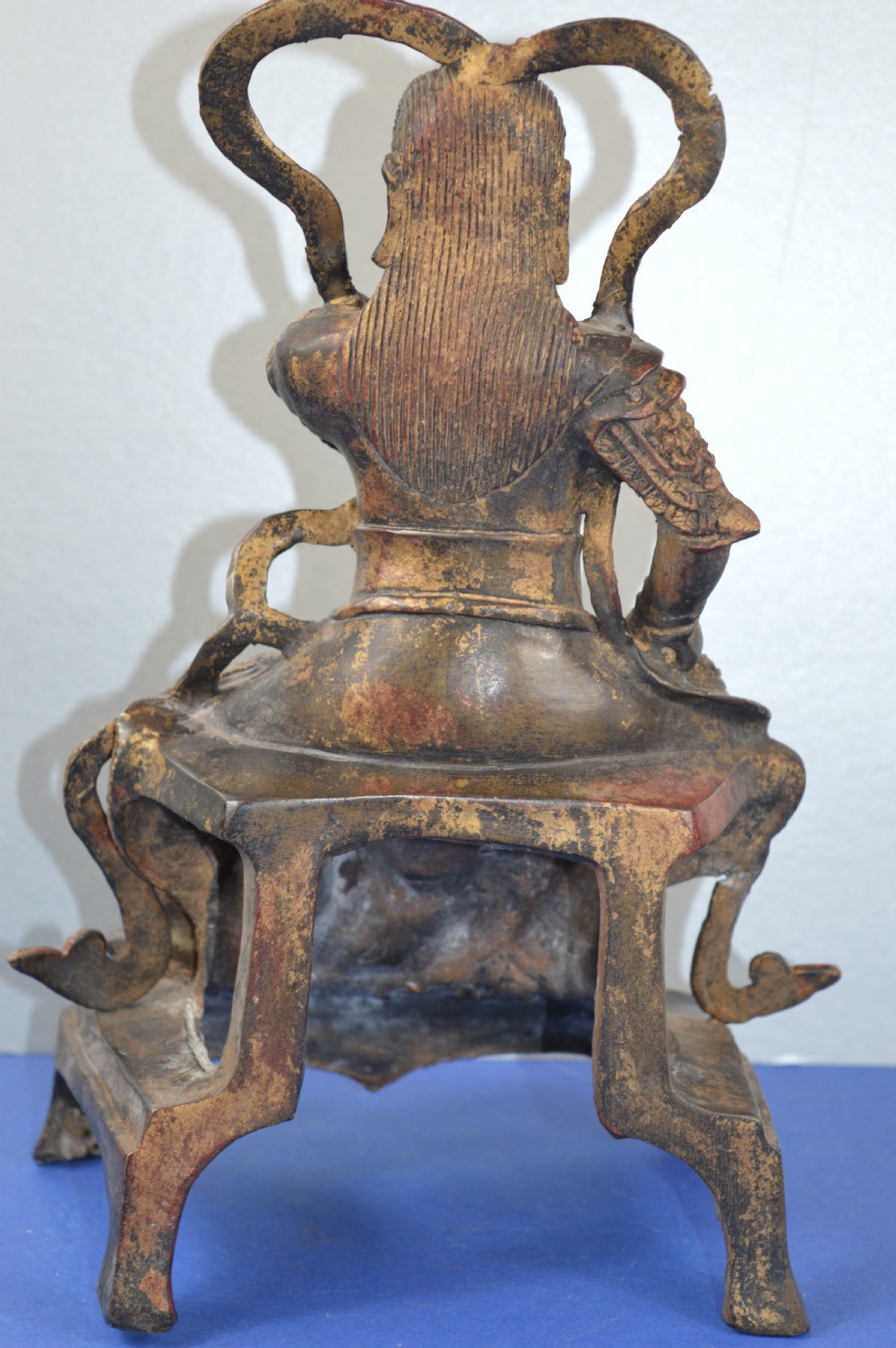 A late nineteenth-century Chinese dark bronze sculpture depicting a seated warrior in detailed armour with polychrome red accents and a decorative halo motif. View V
