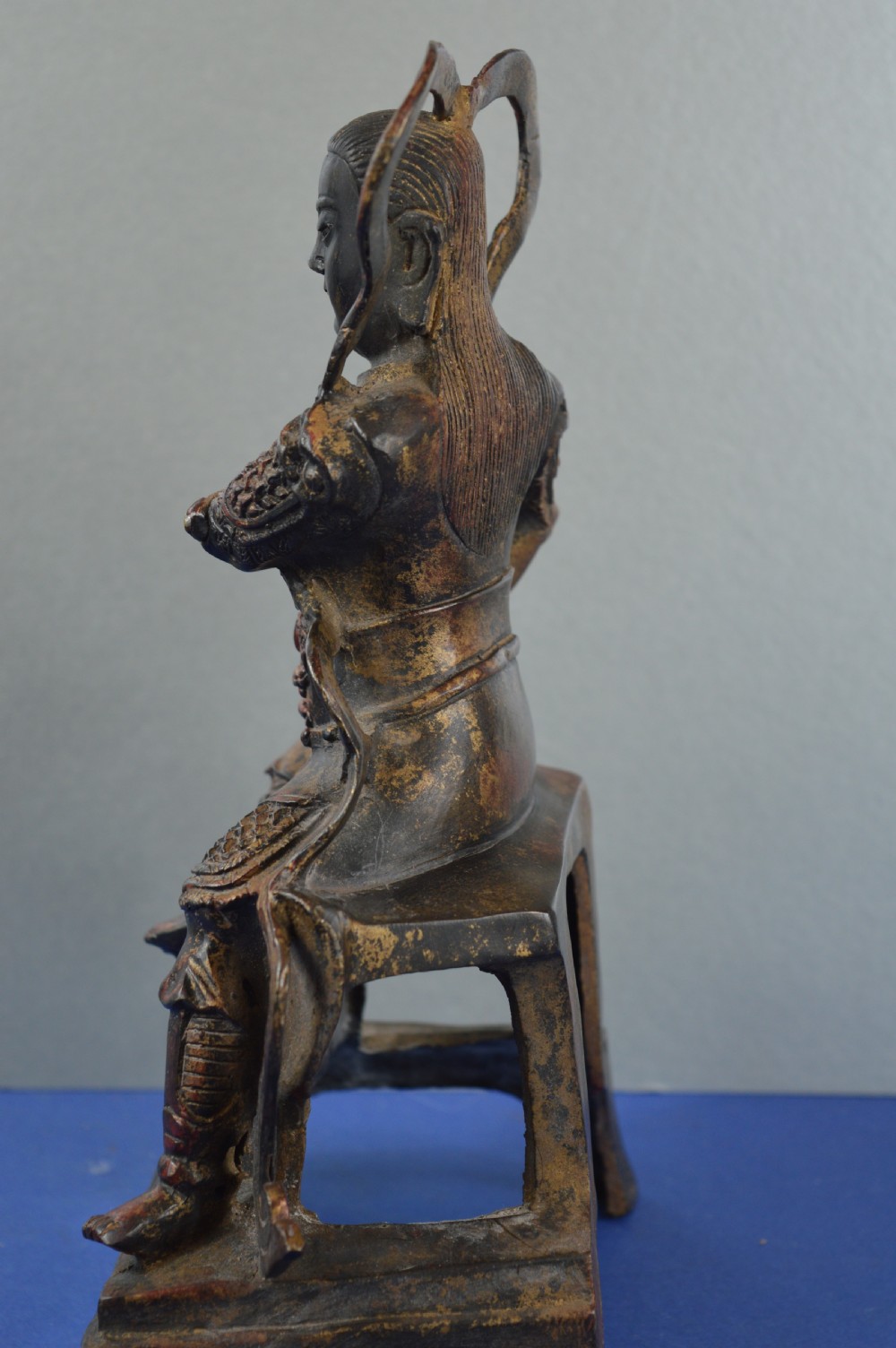 A late nineteenth-century Chinese dark bronze sculpture depicting a seated warrior in detailed armour with polychrome red accents and a decorative halo motif. View VI