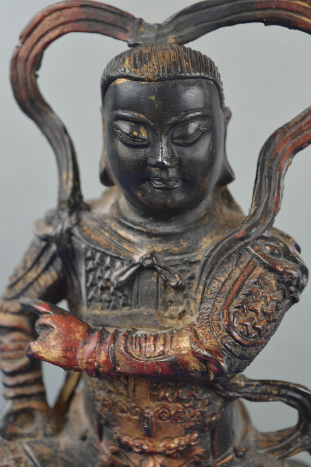 A late nineteenth-century Chinese dark bronze sculpture depicting a seated warrior in detailed armour with polychrome red accents and a decorative halo motif. View VIII