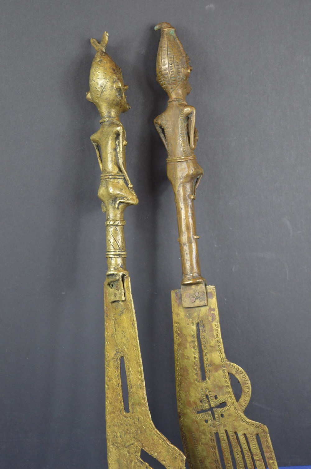 A pair of cast bronze Yoruba ceremonial staffs featuring sculpted human figures as finials above flat, patterned brass blades. View VIII