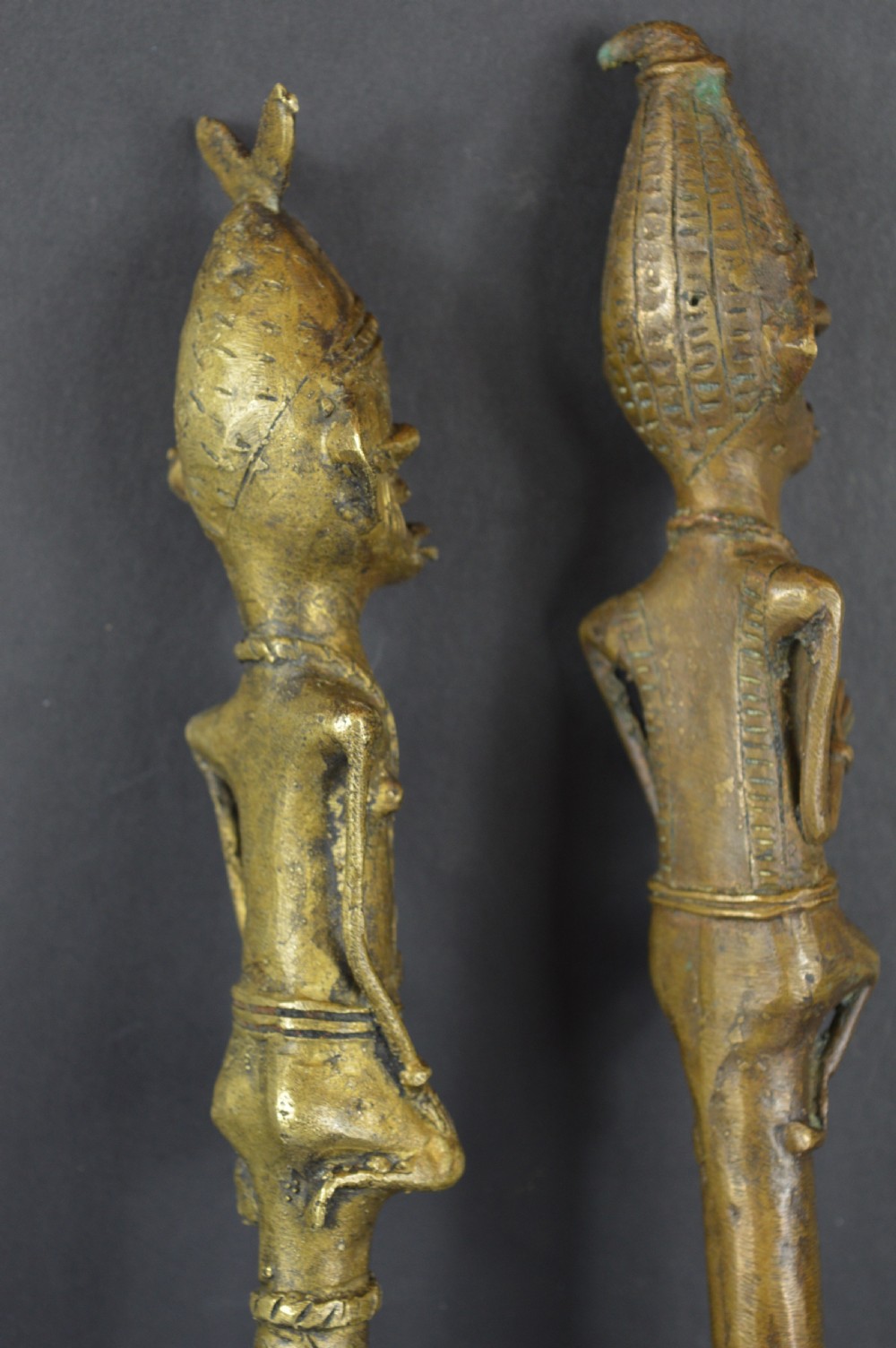 A pair of cast bronze Yoruba ceremonial staffs featuring sculpted human figures as finials above flat, patterned brass blades. View IX