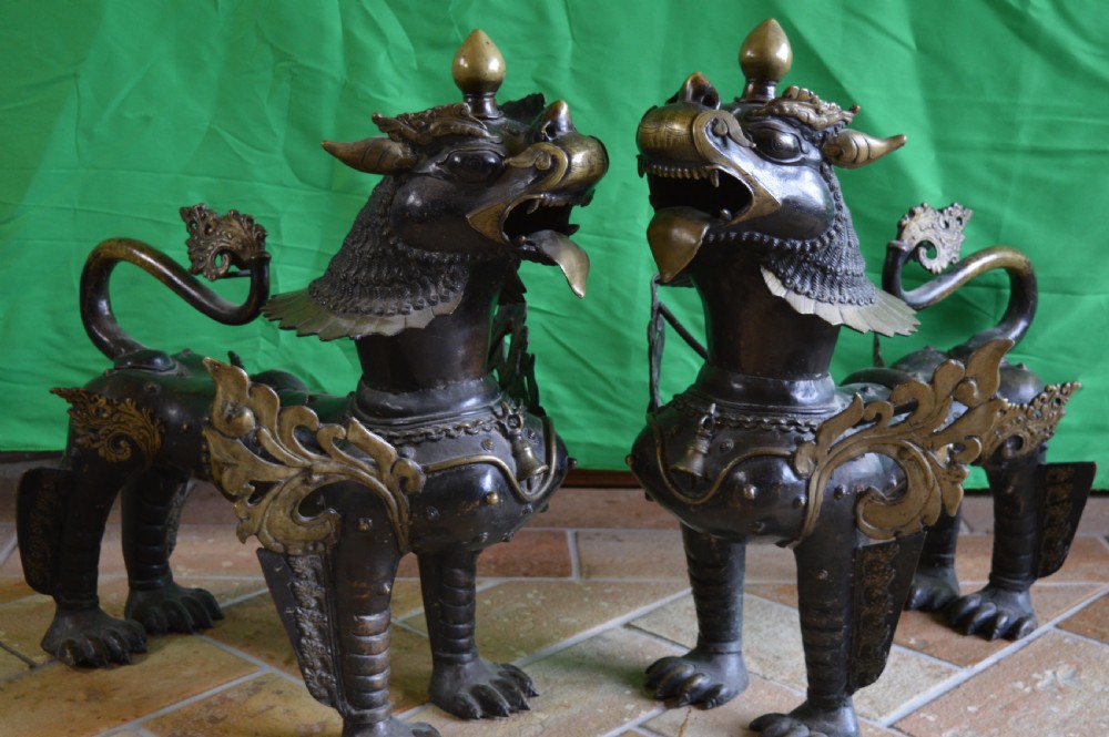 A pair of substantial dark bronze Tibetan temple lions featuring raised tails, stylised scale details, and brass accents.