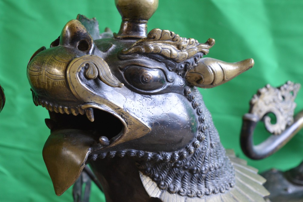 A pair of substantial dark bronze Tibetan temple lions featuring raised tails, stylised scale details, and brass accents. View V