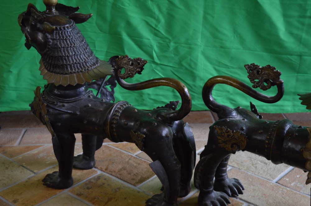 A pair of substantial dark bronze Tibetan temple lions featuring raised tails, stylised scale details, and brass accents. View VII