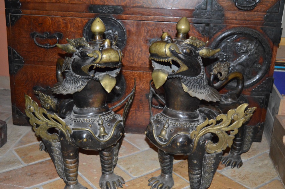 A pair of substantial dark bronze Tibetan temple lions featuring raised tails, stylised scale details, and brass accents. View XX