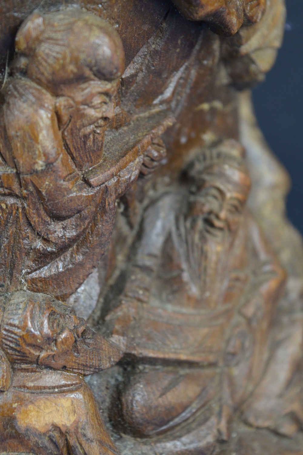 A hand-carved cylindrical bamboo brush pot featuring figures and pine trees carved in high relief against a warm brown wooden surface. View VII