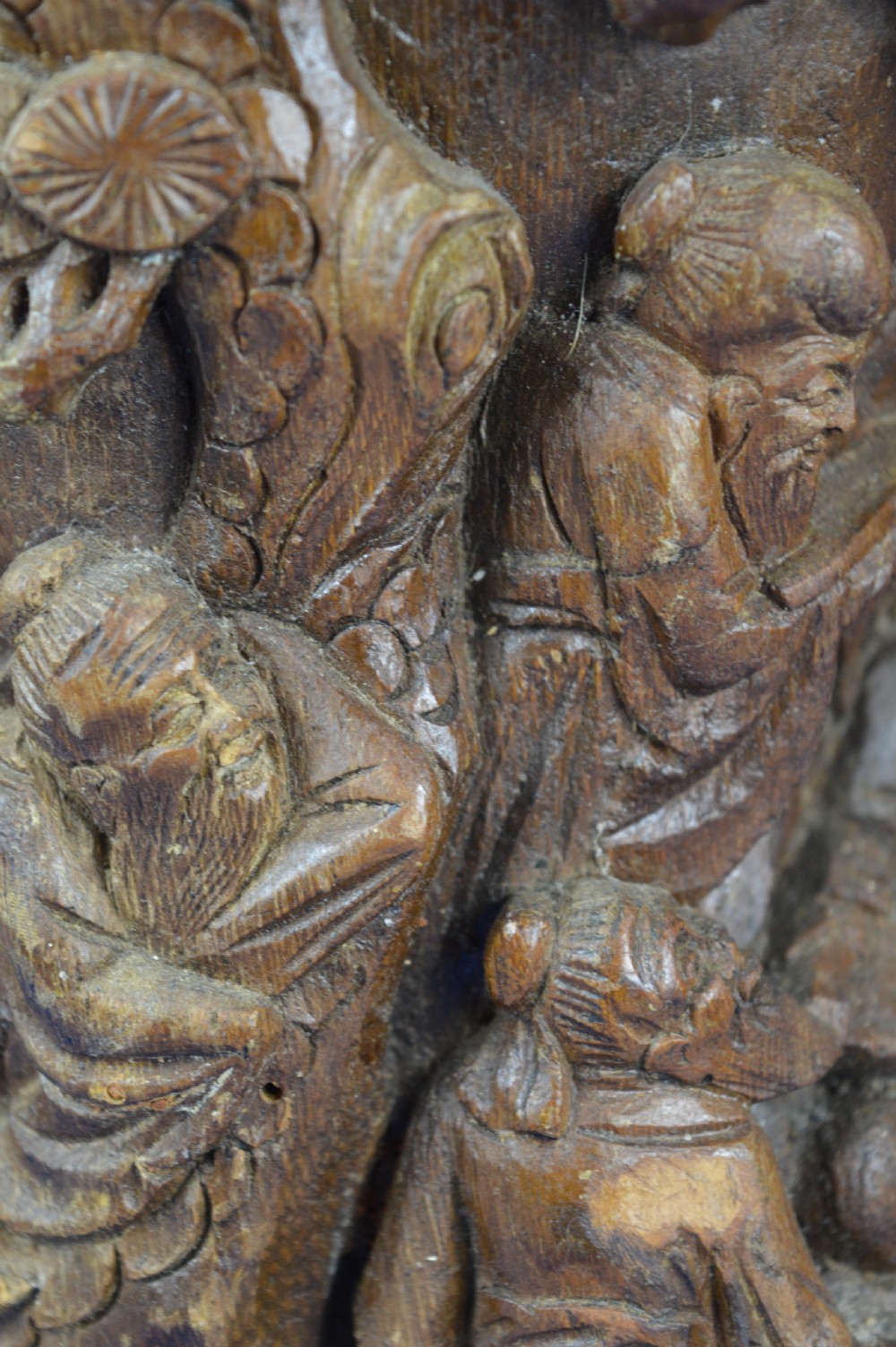 A hand-carved cylindrical bamboo brush pot featuring figures and pine trees carved in high relief against a warm brown wooden surface. View VIII
