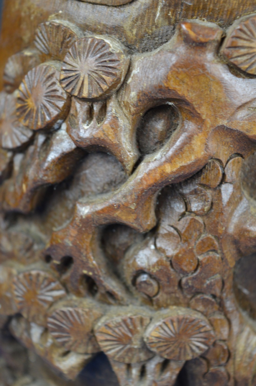 A hand-carved cylindrical bamboo brush pot featuring figures and pine trees carved in high relief against a warm brown wooden surface. View IX