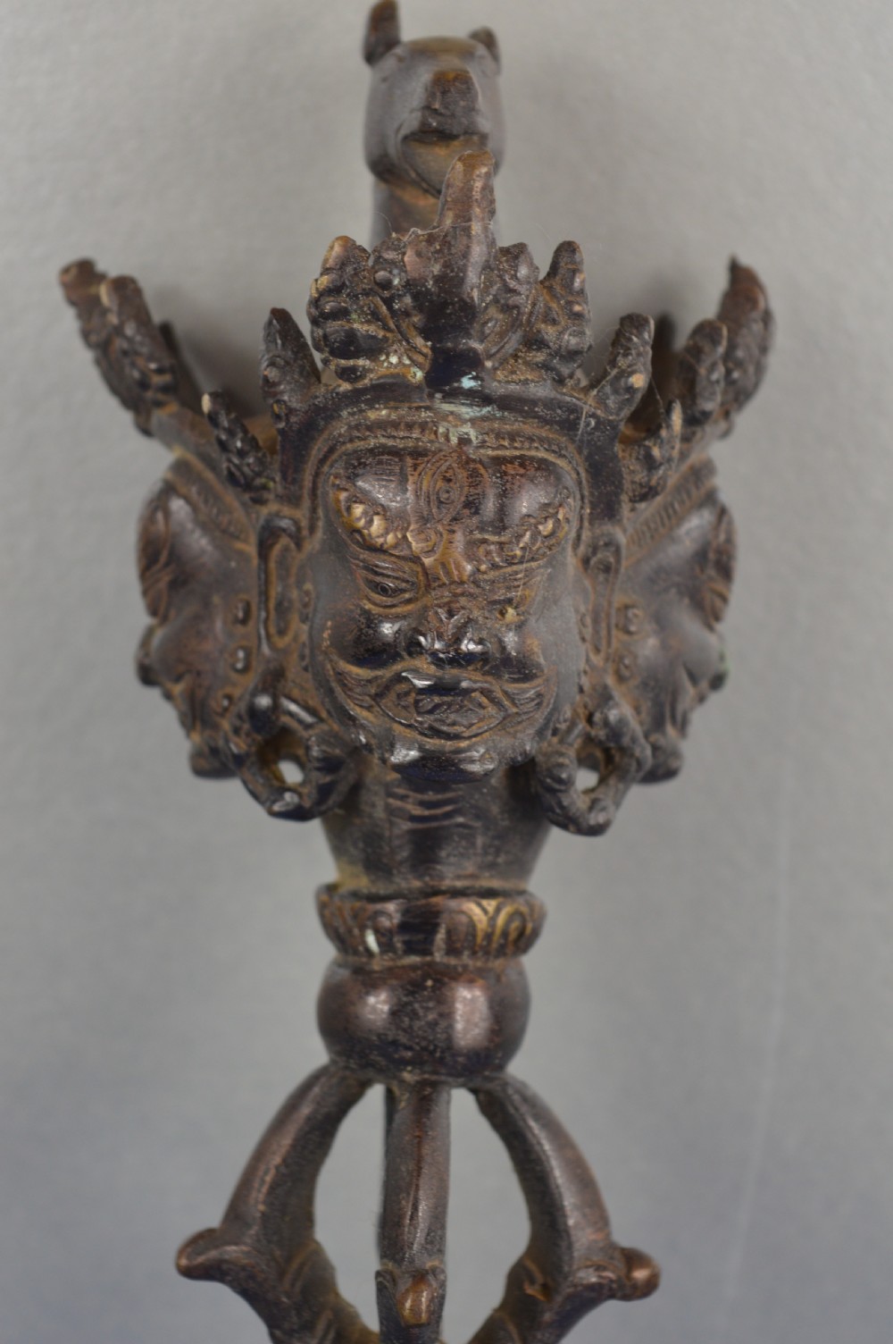 A 19th-century Tibetan bronze phurba featuring a wrathful deity head pommel, central vajra handles, and a three-sided blade extending from a makara mouth. View II