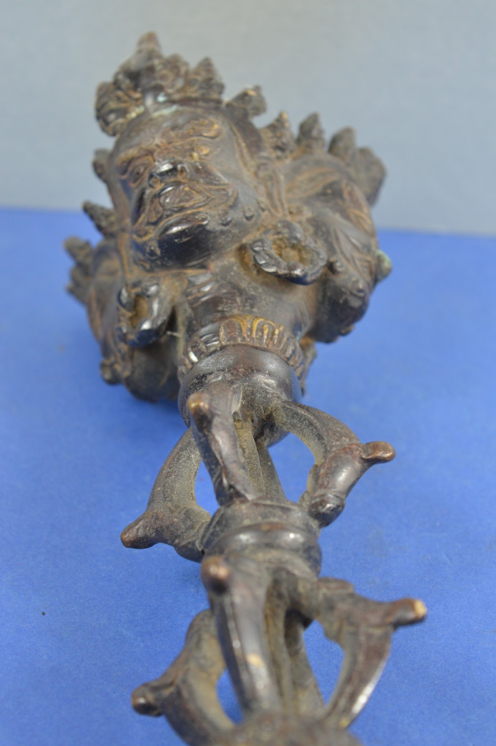 A 19th-century Tibetan bronze phurba featuring a wrathful deity head pommel, central vajra handles, and a three-sided blade extending from a makara mouth. View IX