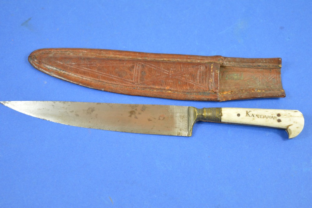 A nineteenth-century Anglo-Afghan war knife featuring a steel blade, a bone handle carved with the word KANDAHAR, and a stamped brown leather sheath.