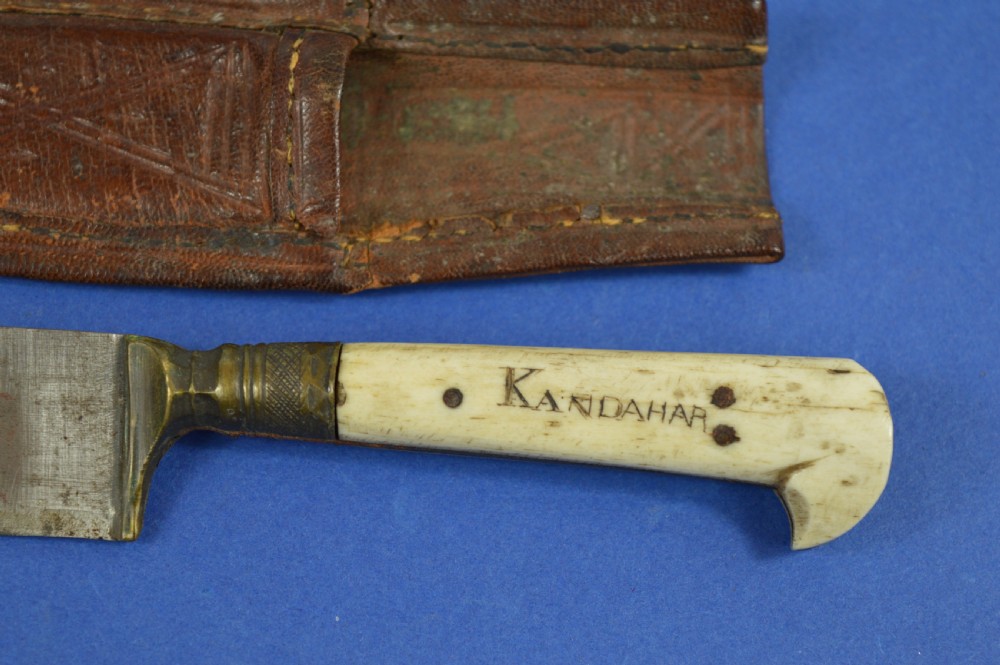 A nineteenth-century Anglo-Afghan war knife featuring a steel blade, a bone handle carved with the word KANDAHAR, and a stamped brown leather sheath. View II