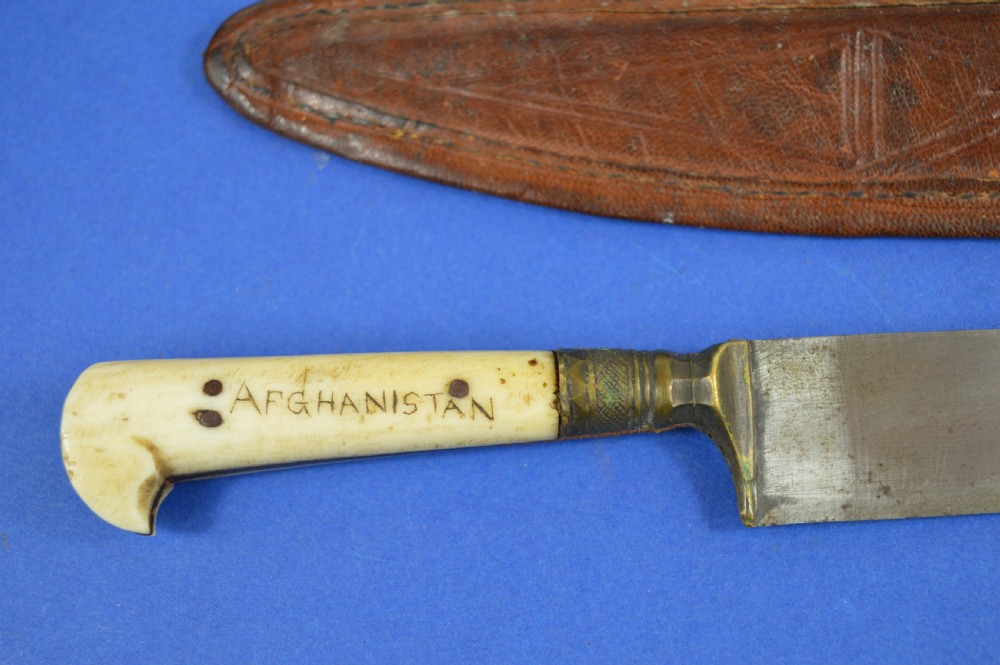 A nineteenth-century Anglo-Afghan war knife featuring a steel blade, a bone handle carved with the word KANDAHAR, and a stamped brown leather sheath. View VI