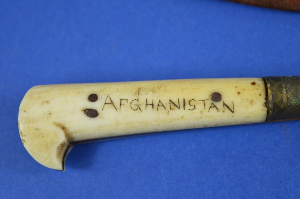 A nineteenth-century Anglo-Afghan war knife featuring a steel blade, a bone handle carved with the word KANDAHAR, and a stamped brown leather sheath. View X